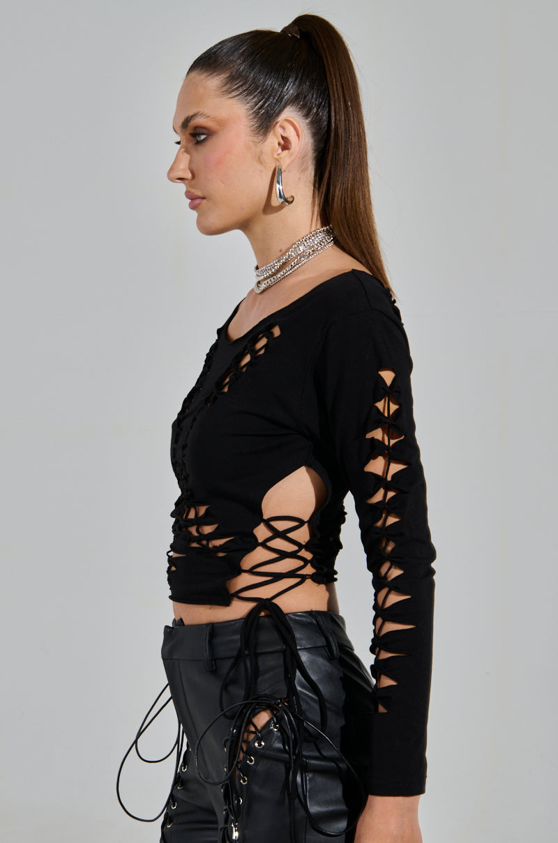 A person with a sexy glimpse sports long brown hair in a high ponytail, wears the RIP ME OUT DISTRESSED LONG SLEEVE TOP in black with crisscross cutouts and matching pants. Silver hoop earrings and a layered necklace complete the look.