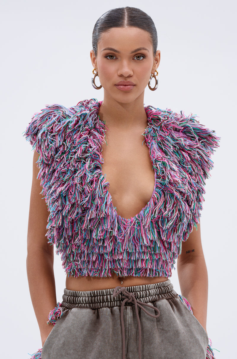 Model wears THE ONE FRINGE BLOUSE featuring a deep V-neck and multicolor fringe, styled with loose gray tie-waist pants and large hoop earrings—an easy yet striking loungewear look against a white background.