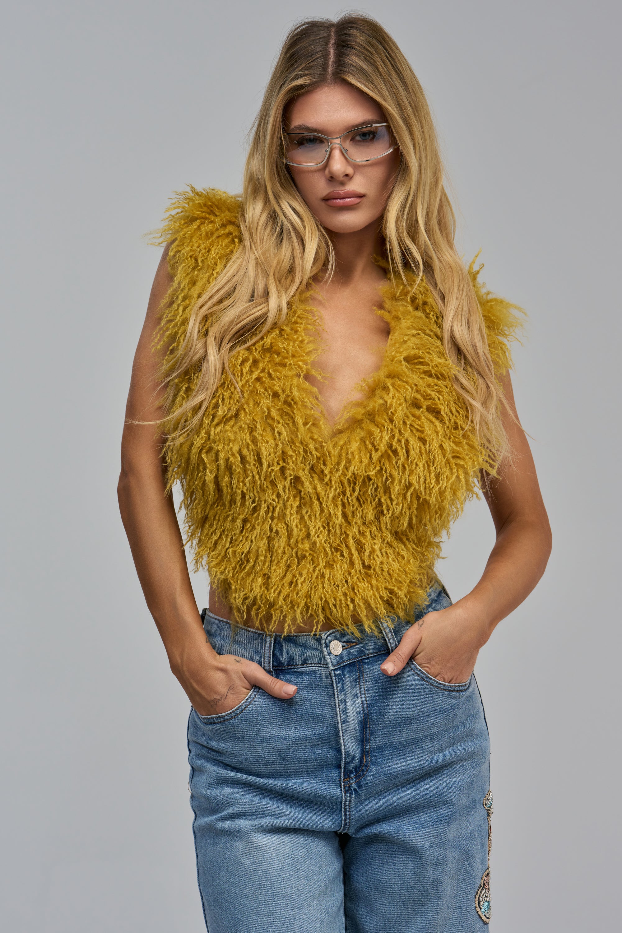 A mustard yellow fuzzy, sleeveless TEMPLETON TOP IN MUSTARD with a deep V-neck and blue jeans, perfect for a girls’ night out.