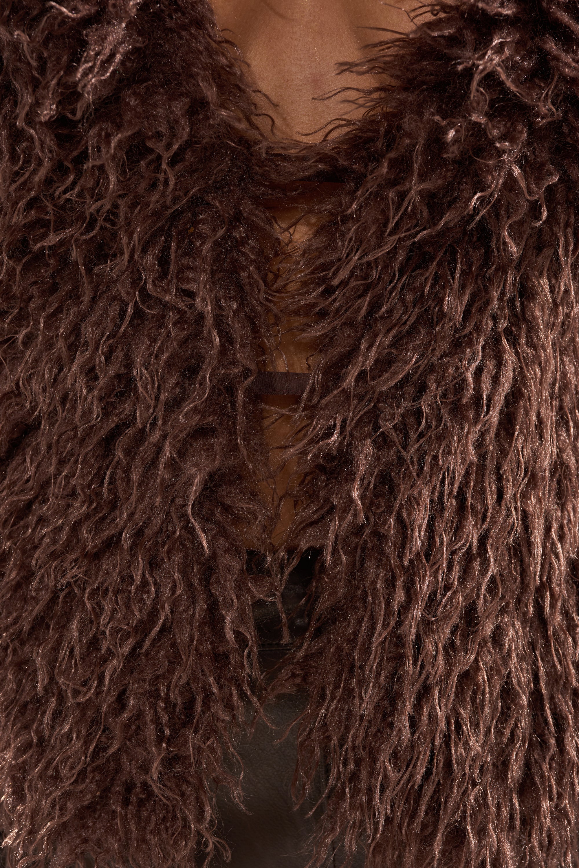 A close-up of someone wearing the HANNAH FUR BLOUSE—a shaggy, textured dark brown faux fur top with crisscrossed straps and an open chest detail—ideal for luxury layering.