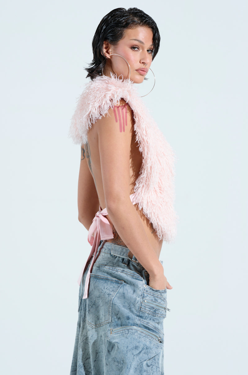 A person with short dark hair models the JAMEELA TOP, a sleeveless pink faux fur halter-style top, paired with light blue jeans. They accessorize with large hoop earrings and display tattoos on their arms, radiating confidence against a plain background. 3