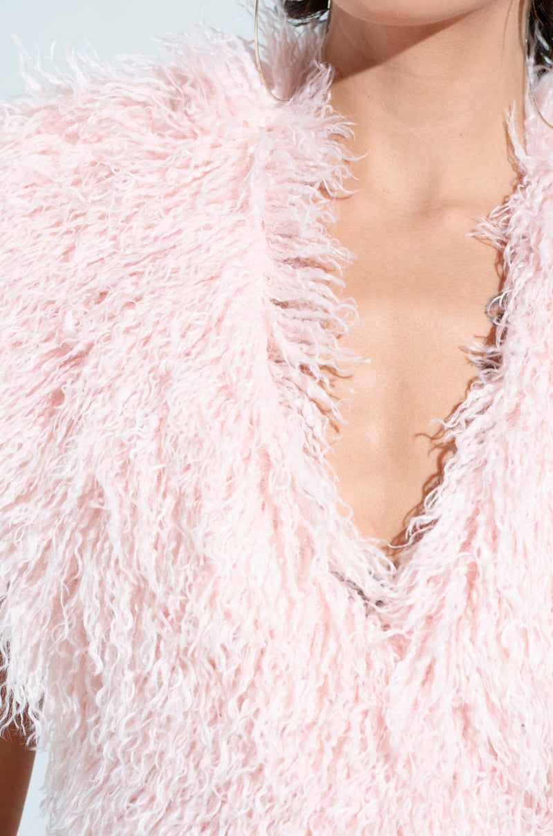 A person wears the JAMEELA TOP, a textured, fluffy pink faux fur top with a plunging V-neckline. Only part of their face and hair is visible, accompanied by a large hoop earring, highlighting the soft and feathery fabric. 8