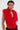 A person with short dark hair wears the CARLA FAUX FUR HALTER TOP—a fluffy red faux fur piece with a plunging V-neckline—styled with gold layered necklaces, hoop earrings, and dark pants against a plain light background.