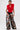 A person wears the CARLA FAUX FUR HALTER TOP in bright red, styled with wide-leg black pants featuring bold playing card and artistic face prints, against a plain white background.