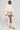 Clad in the NOT YOUR NORMAL BIKER CHICK TOP, meticulously buttoned up with a high collar, and beige shorts, the individual stands confidently. They accessorize with a matching bag, faux leather boots, and leg warmers. Sunglasses complete their stylish, modern look.