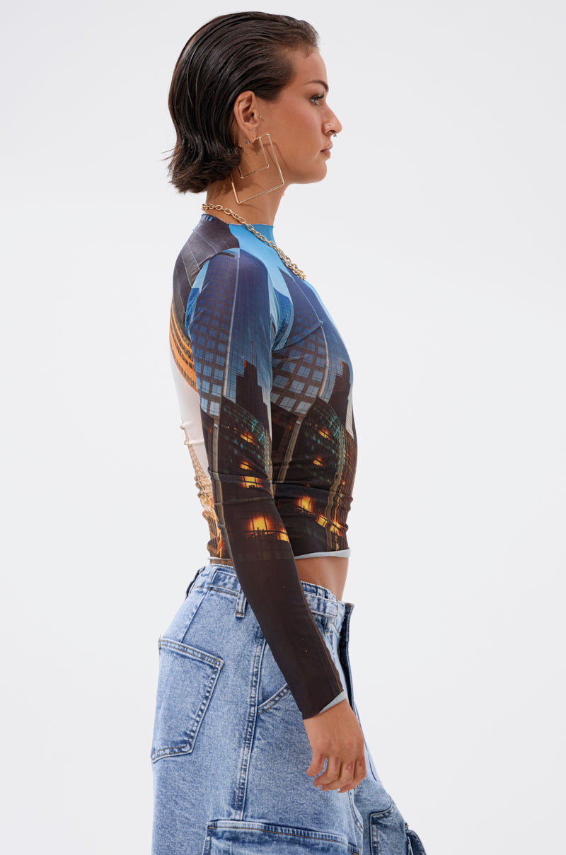 A woman with short, slicked-back hair is shown in profile against a plain white background, wearing the BIG CITY LONG SLEEVE MESH TOP paired with high-waisted blue jeans. 2