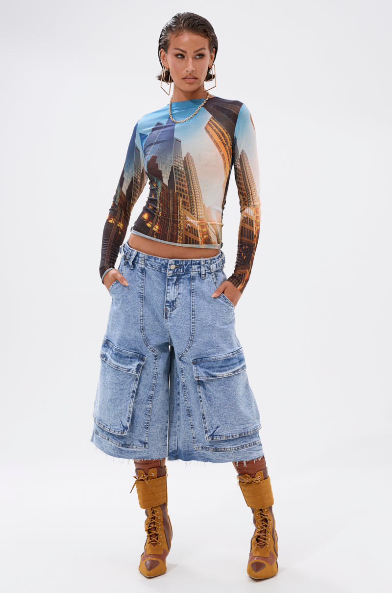 A woman stands confidently in the BIG CITY LONG SLEEVE MESH TOP, loose light denim cargo shorts, and tan lace-up boots against a plain white background. 6
