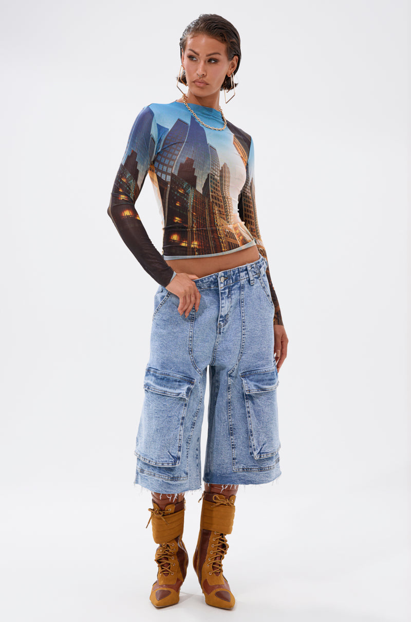 A woman stands confidently in the BIG CITY LONG SLEEVE MESH TOP, paired with loose light blue knee-length frayed denim shorts and brown lace-up boots against a plain white background. 7