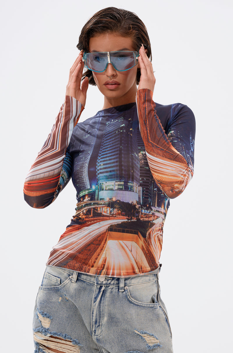 A woman in light blue sunglasses, the CITY LOVER MESH LONG SLEEVE top, and ripped jeans poses confidently against a plain white background. 0