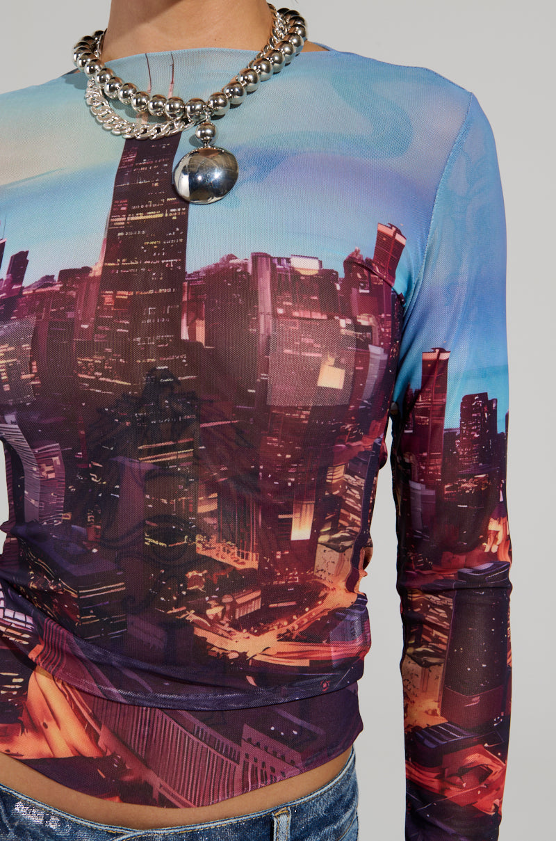 A person wearing the CITYSCAPE TOP, a fitted long-sleeve shirt adorned with a graphic of the Chicago skyline featuring skyscrapers and urban lights. The top captures urban-chic fashion, complemented by a chunky silver chain necklace.