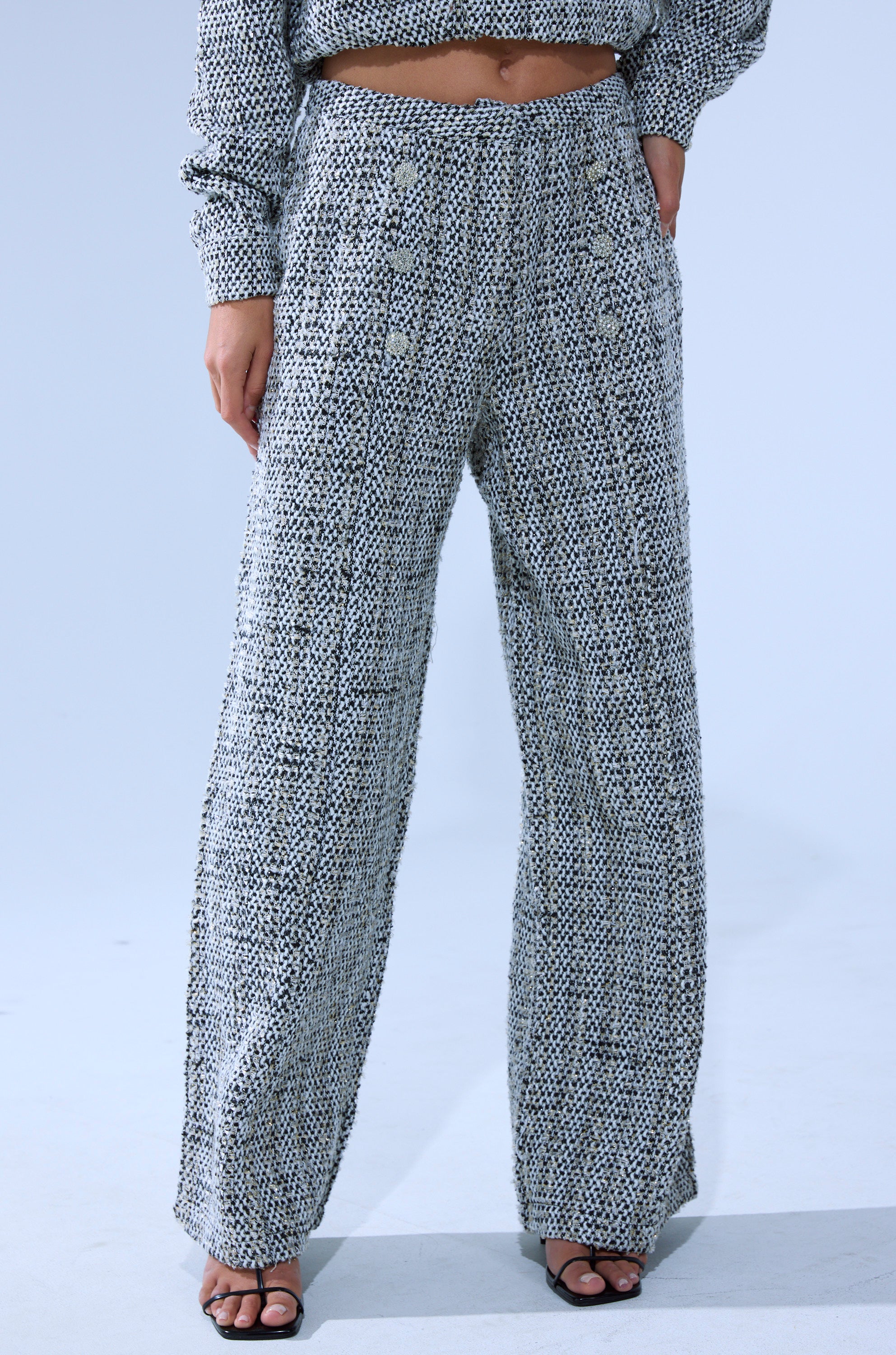Wearing the DRESSY VIBES TWEED PANT, a person shows off its high-rise, wide-leg fit with decorative buttons and pairs it with a matching cropped sweater and black open-toe heels, posing on a light background. 2