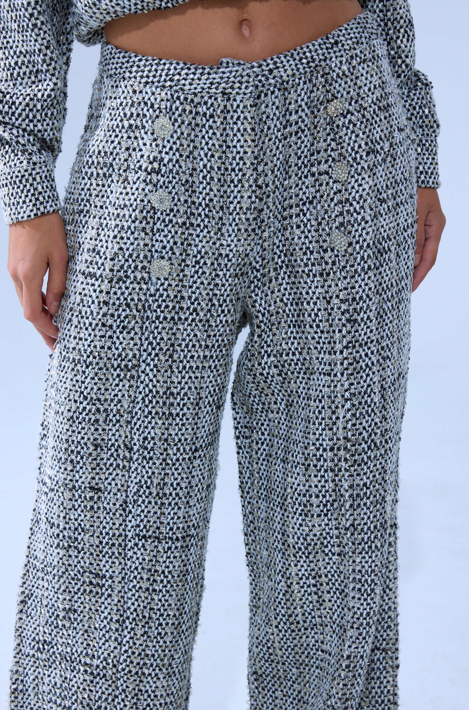 A person wears the DRESSY VIBES TWEED PANT featuring a high-rise, wide-leg knit design with a textured black and white pattern and decorative buttons, paired with a matching knit top. 8