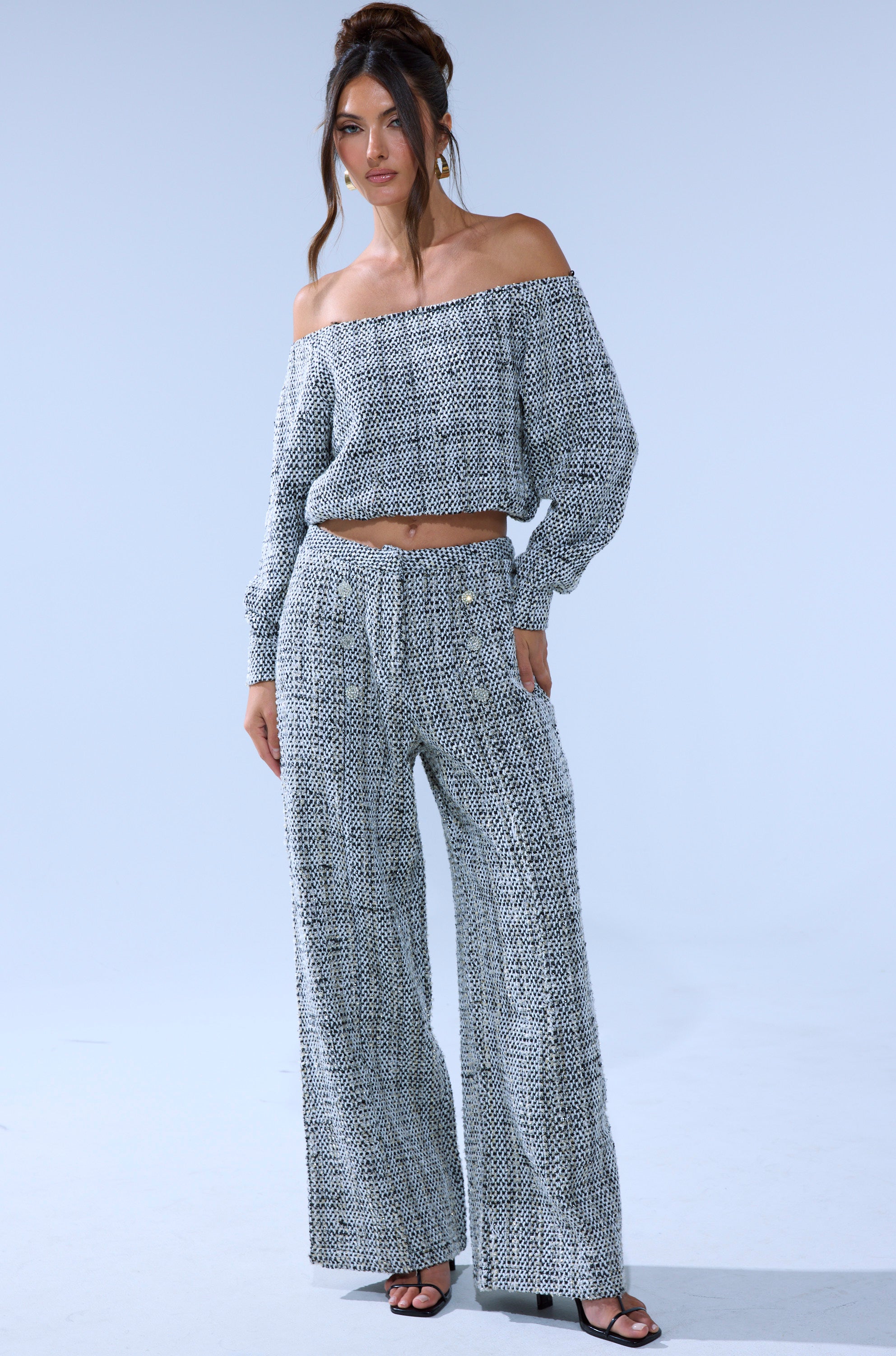 A woman wears the Dressy Vibes Off The Shoulder Sweatshirt with matching wide-leg pants and black heeled sandals, standing against a plain light blue background.