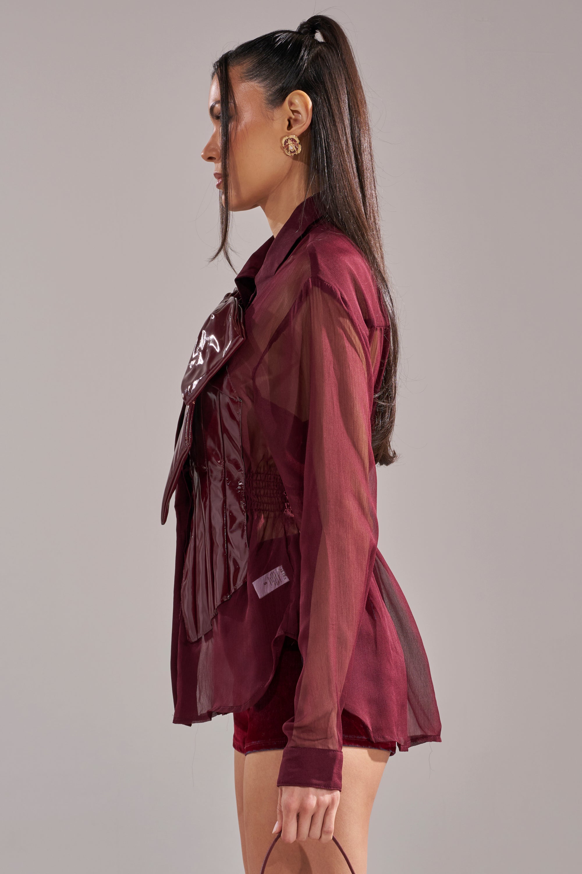 A woman with long brown hair in a high ponytail wears the CRAZY FOR YOU CHIFFON BUTTON DOWN blouse and matching shorts, holding a small handbag while standing in profile against a plain background.