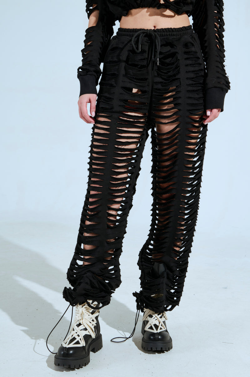 A person wears black CLEAN LINES SLASHED PANT and a matching high-rise top with numerous horizontal rips, paired with black and white lace-up boots on a light background. 2