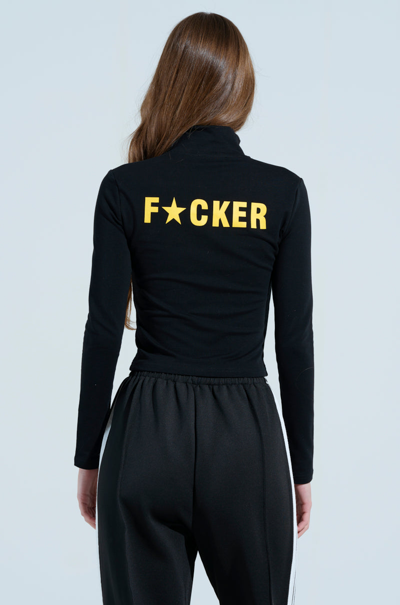 A person with long hair faces away, wearing the AKIRA Label's black "MOTHER F*UCKER" zip-up sweatshirt featuring yellow letters on the back, paired with black pants and white side stripes. A light blue background provides a cool contrast.