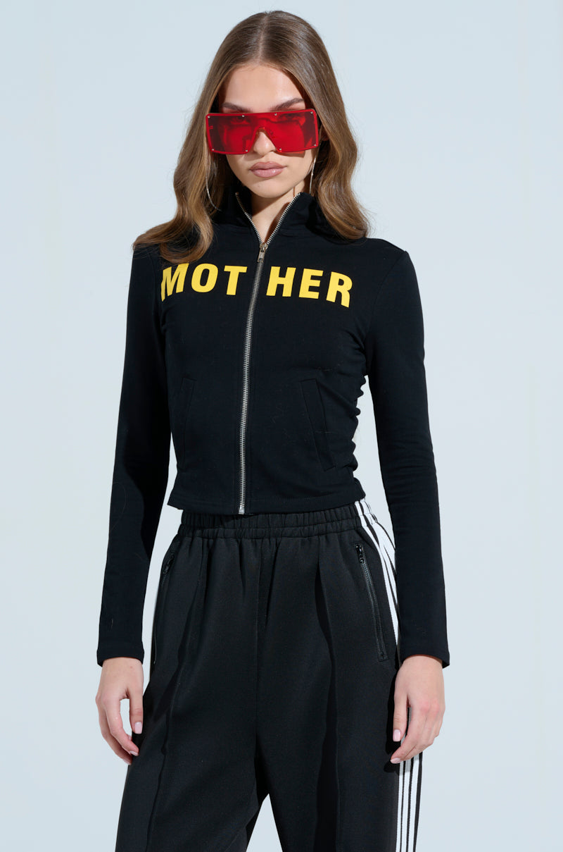 A person is wearing the AKIRA Label's MOTHER F*UCKER ZIP UP SWEATSHIRT, black pants with white stripes, and large red sunglasses. They have long hair and are set against a solid light blue background.