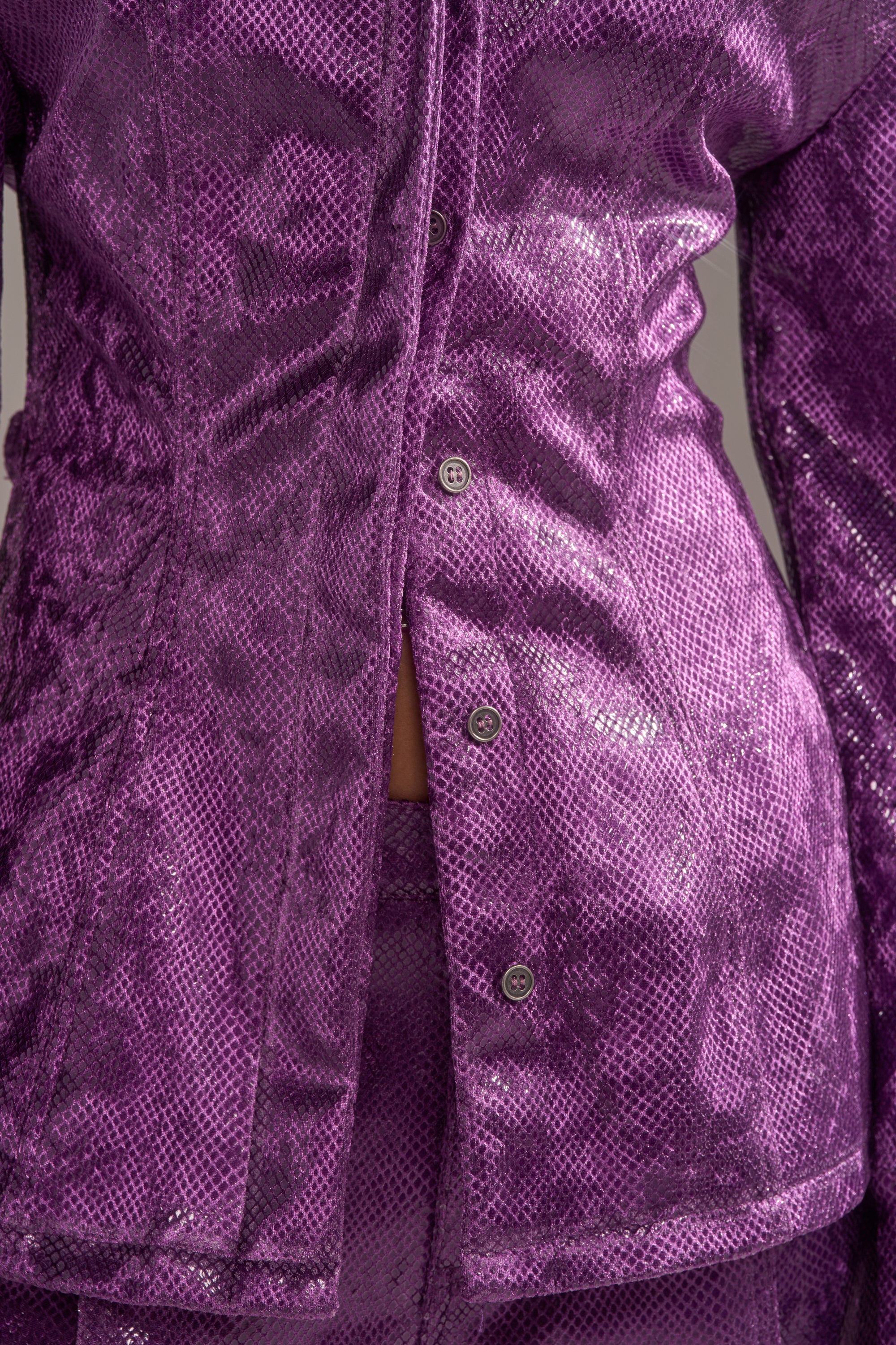 A close-up shows someone in the CRAZY TOUCH VELVET BUTTON DOWN, a shiny, textured purple snakeskin print top with matching pants. The jacket is partially unbuttoned to reveal a hint of midriff for a bold, stylish look. 8