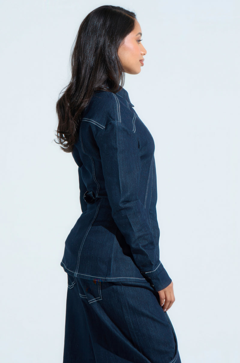 A person with long dark hair models the COME WITH ME BUTTON DOWN TOP and a matching skirt, featuring an oversized relaxed silhouette, as they stand in profile against a light neutral background.