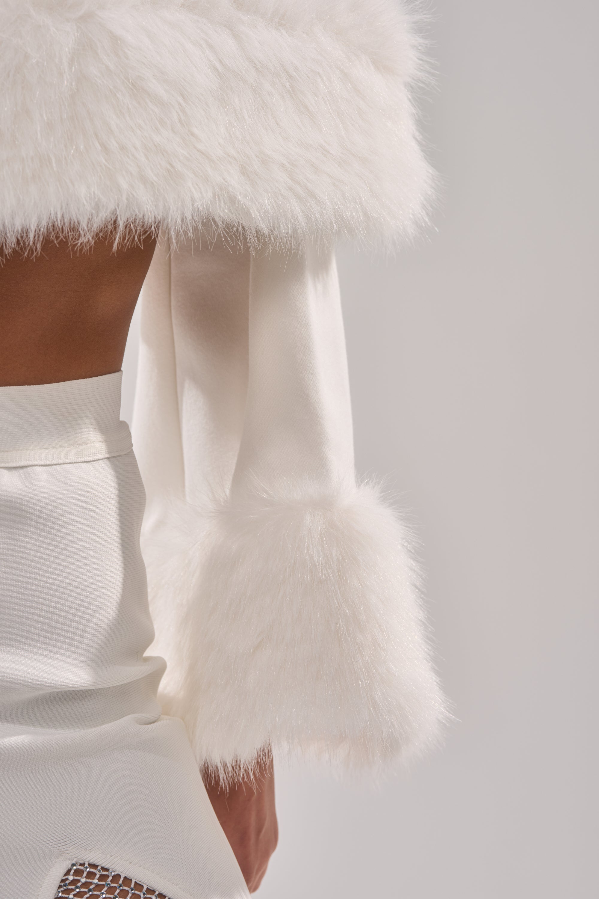 A close-up shows a person wearing the SNOW BUNNY FUR BLOUSE—a white, long-sleeve top with fluffy fur accents on the cuffs and shoulders—paired with a high-waisted skirt, set against a neutral background.