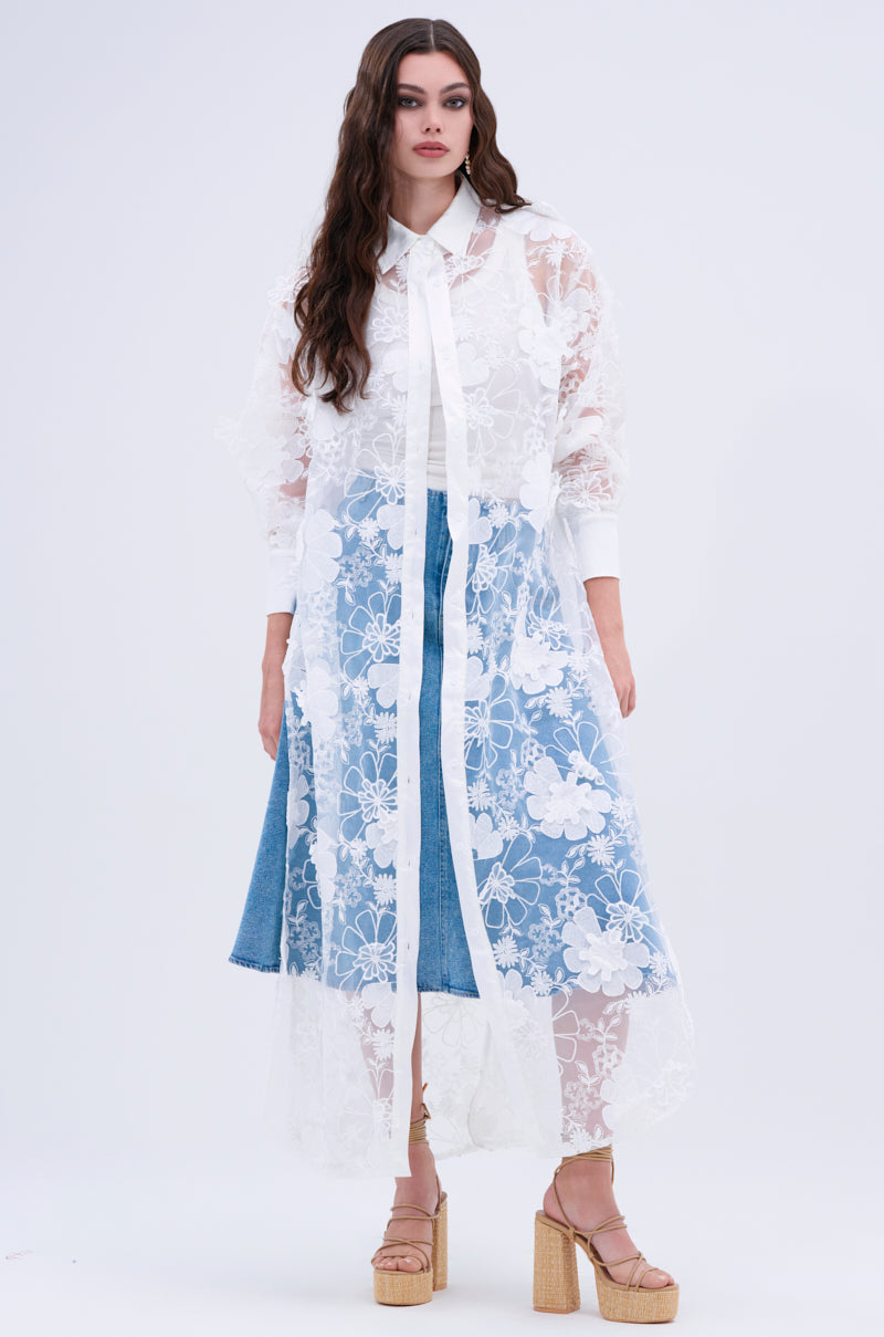 A woman stands against a plain background wearing the LACE BUTTON UP blouse over a blue denim skirt and white shirt, paired with beige platform sandals.