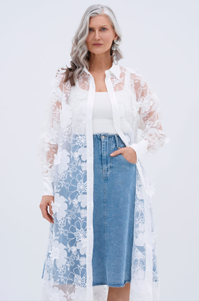 A woman with long gray hair wears the LACE BUTTON UP over a white top and high-waisted denim skirt, standing confidently with one hand in her pocket against a plain light background.