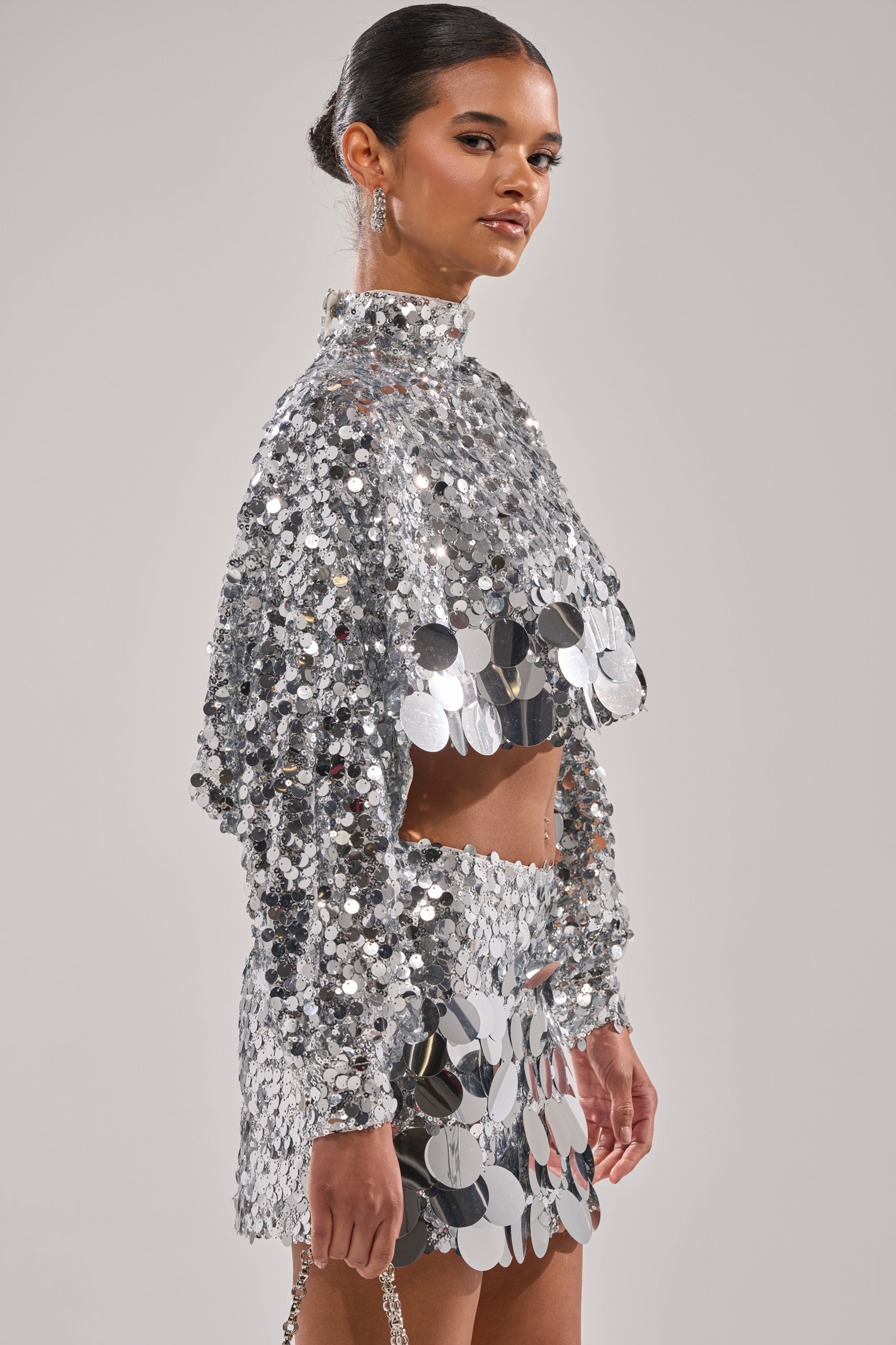 A woman models the HOLIDAY BLING SEQUIN BLOUSE, a shiny, cropped, long-sleeved top covered in large silver sequins for a dazzling, reflective style.