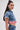 A woman with long dark hair in a high ponytail wears the FULL OF LIFE DENIM BUTTON DOWN WITH PLAID DETAILS, styled with high-waisted denim jeans.