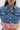 A woman models the FULL OF LIFE DENIM BUTTON DOWN WITH PLAID DETAILS, featuring large silver buttons, front pockets, and a frayed hem with colorful plaid trim in a boxy cropped silhouette from shoulders to waist.