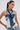 A woman with long brown hair in a ponytail, large hoop earrings, and a sleeveless ALWAYS RIGHT DENIM ABSTRACT BLOUSE with frayed edges and corset-style silhouette stands against a plain light background.