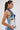 A woman with long dark hair in a ponytail wears large hoop earrings and the ALWAYS RIGHT DENIM ABSTRACT BLOUSE, a strapless patchwork denim corset-style top with a visible brown label, paired with jeans, standing in profile against a plain background.
