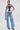 A woman poses confidently in the ALWAYS RIGHT DENIM ABSTRACT BLOUSE, a patchwork mixed-wash denim top with a corset-style silhouette, paired with high-waisted wide-leg jeans, a small silver bag, and heeled sandals against a white background.