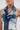 A woman wears large hoop earrings and the ALWAYS RIGHT DENIM ABSTRACT BLOUSE, a sleeveless halter top featuring patchwork mixed-wash denim, frayed edges, and layered details. Her face is partly visible against a plain white background.