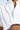 Close-up of a person wearing the SHINE ON BUTTON DOWN BUBBLE TOP, a white short-sleeve shirt with a slightly open chest and an elastic bubble hem gathered at the waist to reveal part of the midriff.