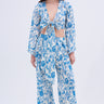 A woman with long, wavy brown hair and a neutral expression stands against a plain background wearing the DOLLED UP PALAZZO PANT—a vintage floral print set featuring a deep V-neck, tie-front top with cutouts, and high-waisted palazzo pants.