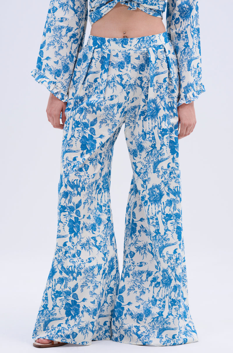 Someone stands against a plain background, midriff exposed, dressed in DOLLED UP PALAZZO PANT with a high-rise waistband and blue & white vintage floral print, paired with a matching top.
