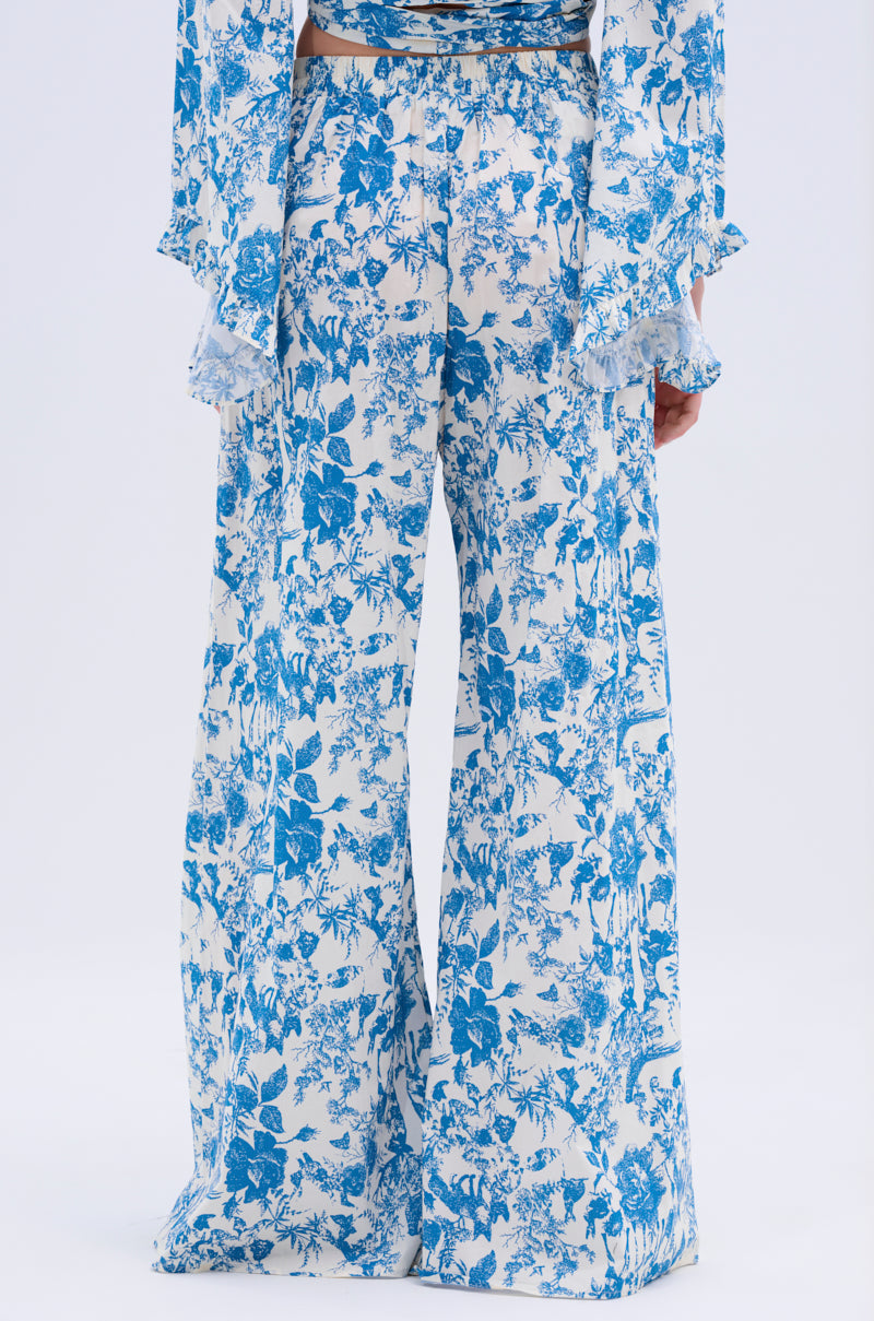 Someone wearing the DOLLED UP PALAZZO PANT, featuring a vintage blue and white floral print and high-rise waistband, seen from the back. The pants are paired with a matching ruffled-sleeve top.