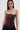 A woman with straight brown hair wears the WILD WEST CORSET TOP, a strapless faux leather top with a sweetheart neckline, paired with dark jeans. She faces forward against a plain light background.