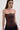 A woman with long brown hair wears the WILD WEST CORSET TOP, a strapless faux leather piece with a sweetheart neckline, paired with dark denim jeans. She stands against a white background, looking at the camera with a neutral expression.