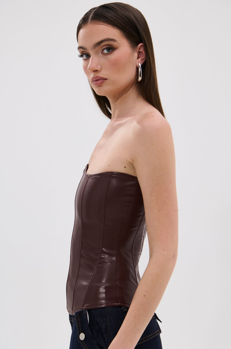 A woman with straight brown hair wears the WILD WEST CORSET TOP in dark brown and dark jeans. She faces sideways, looking at the camera, with silver hoop earrings against a plain light background. 2