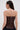 A woman with straight brown hair wears the WILD WEST CORSET TOP, a strapless design with sweetheart neckline and visible back zipper, paired with silver hoop earrings, standing against a plain light background.