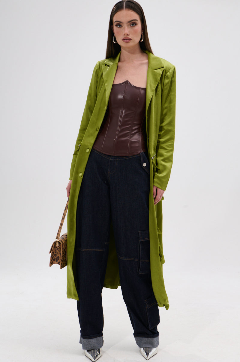 A woman wears the WILD WEST CORSET TOP in brown faux leather with a sweetheart neckline, styled with a long lime green trench coat, wide-leg dark jeans, pointed silver shoes, and a leopard print bag against a white background. 4