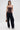 A woman poses against a plain background in the WILD WEST CORSET TOP, featuring a strapless faux leather design with a sweetheart neckline, styled with cuffed dark wide-leg jeans, silver pointed shoes, hoop earrings, and an animal print handbag.