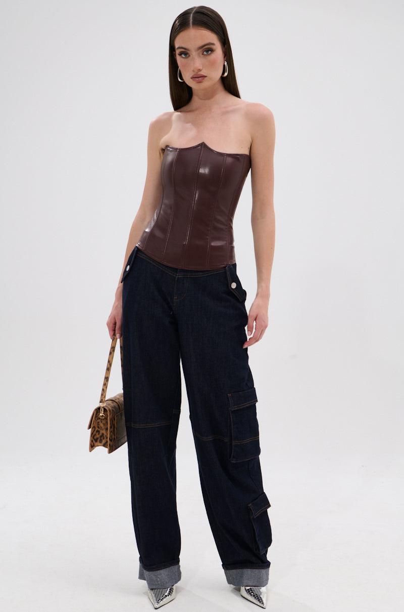 A woman stands against a white background wearing the WILD WEST CORSET TOP, a strapless faux leather corset with a sweetheart neckline, styled with wide-leg dark denim cargo pants, silver pointed-toe heels, hoop earrings, and an animal print handbag. 6
