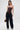A woman stands against a white background wearing the WILD WEST CORSET TOP, a strapless faux leather corset with a sweetheart neckline, styled with wide-leg dark denim cargo pants, silver pointed-toe heels, hoop earrings, and an animal print handbag.