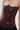 A person wearing the WILD WEST CORSET TOP—a shiny brown, strapless corset with visible seams and a sweetheart neckline—paired with dark blue pants, shown from shoulders to hips.
