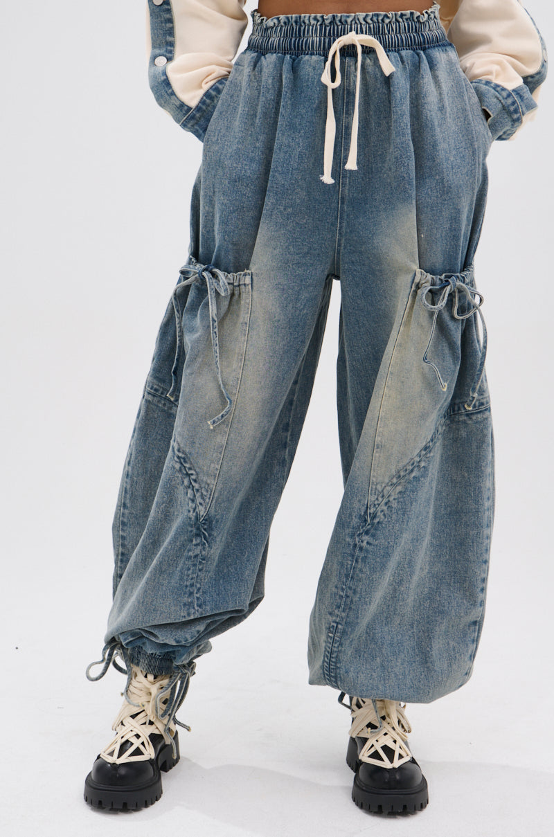 Wearing the RELAX WITH WITH ME JOGGER—loose-fit, vintage-washed denim cargo pants with large side pockets, drawstring details, and elastic cuffs—paired with chunky white lace-up boots. Upper body mostly out of frame.