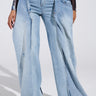 A person flaunts SEEING DOUBLE DECONSTRUCTED DENIM JEANS, featuring a high-rise fit with double-layered wide-leg denim and an overlapping design. The light blue jeans, with exaggerated flares and layered waistbands, perfectly complement a dark long-sleeve top and open-toe heels.