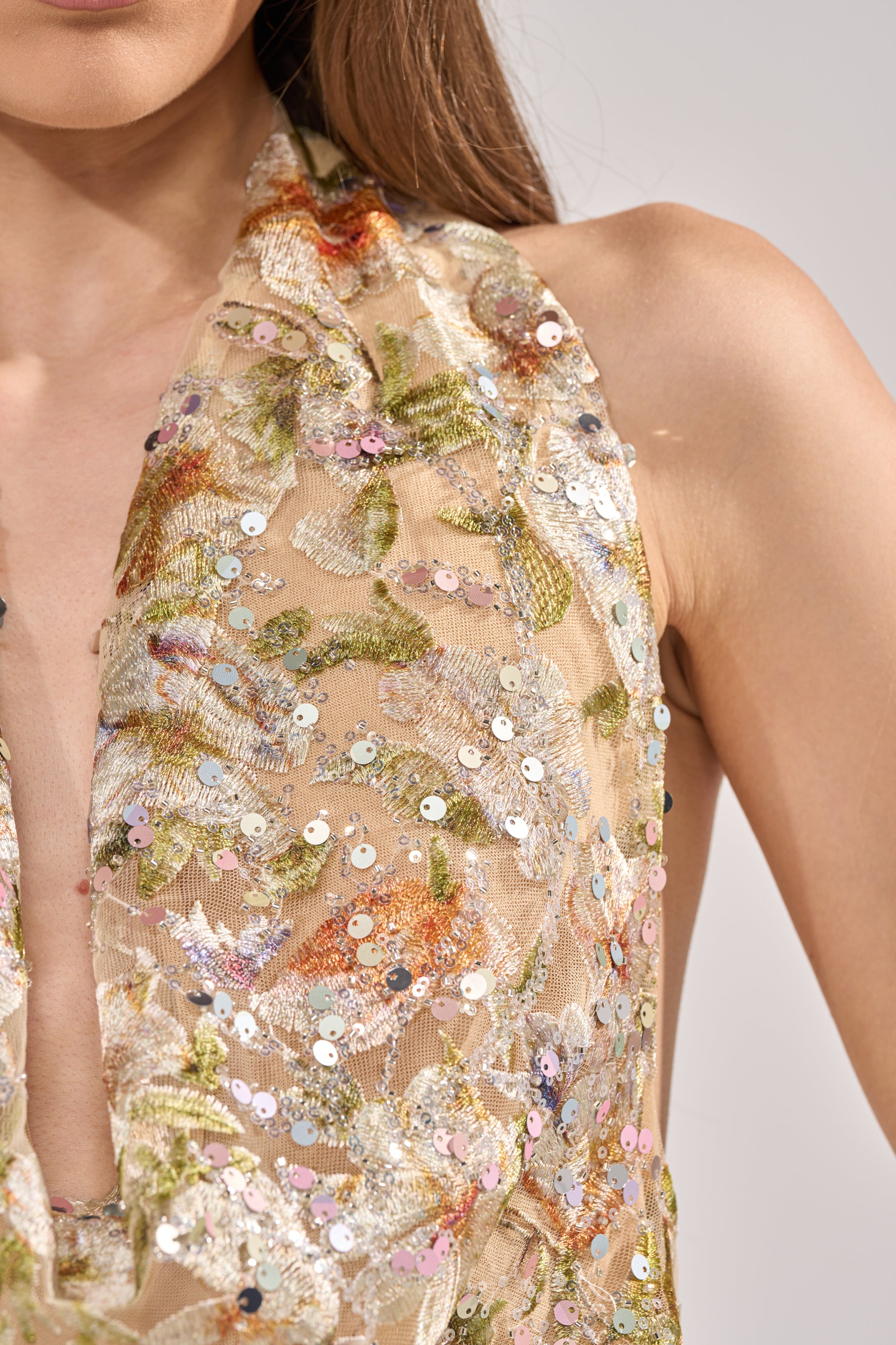 Close-up of a woman's shoulder and upper chest wearing the LETS TALK ABOUT IT COWL NECK, featuring sheer beige mesh with floral embroidery and multicolored sequins. The background is plain and light-colored. 10