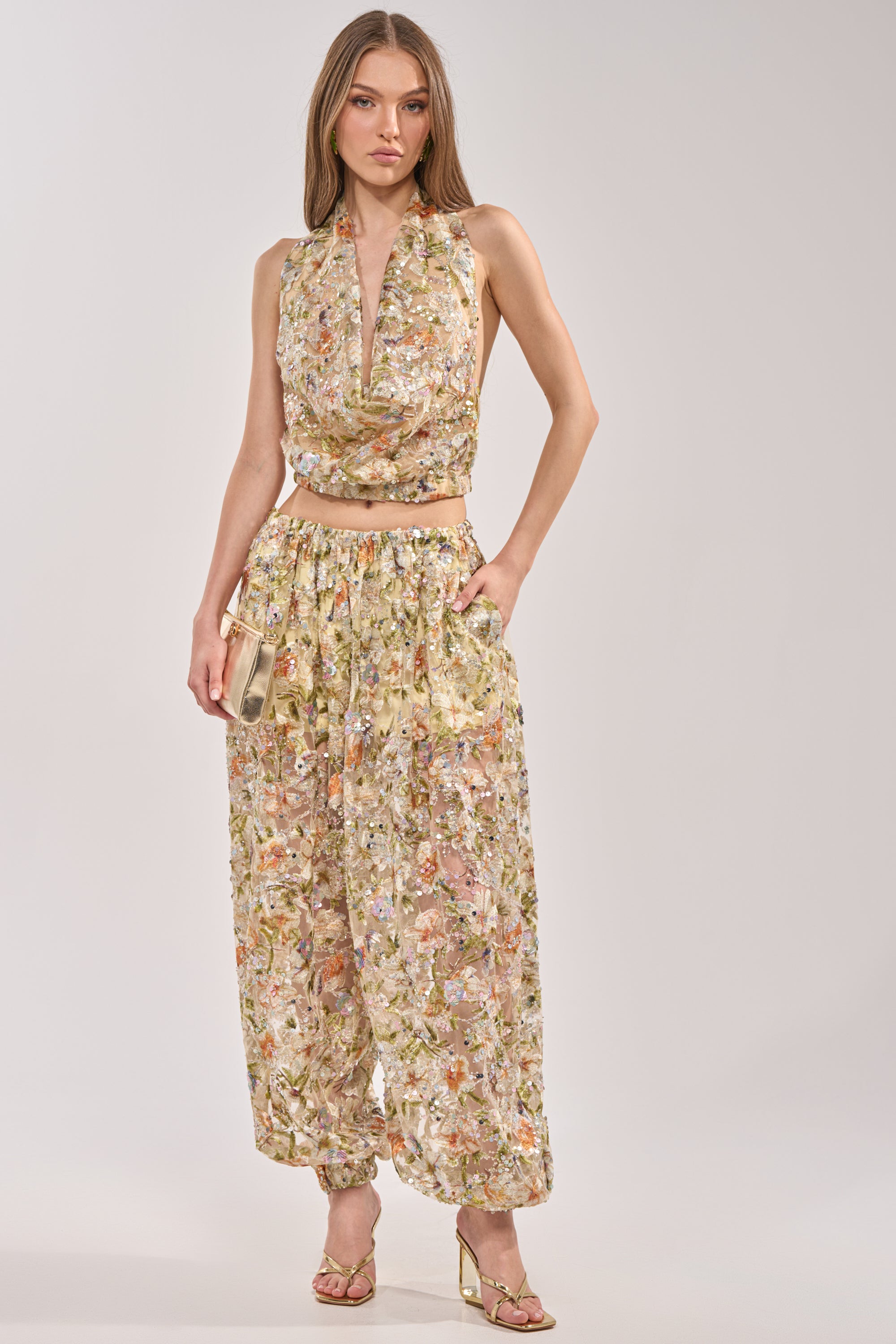 A woman wears the LETS TALK ABOUT IT COWL NECK top with matching high-waisted pants and heeled sandals, holding a metallic clutch. She stands against a plain light background. 8